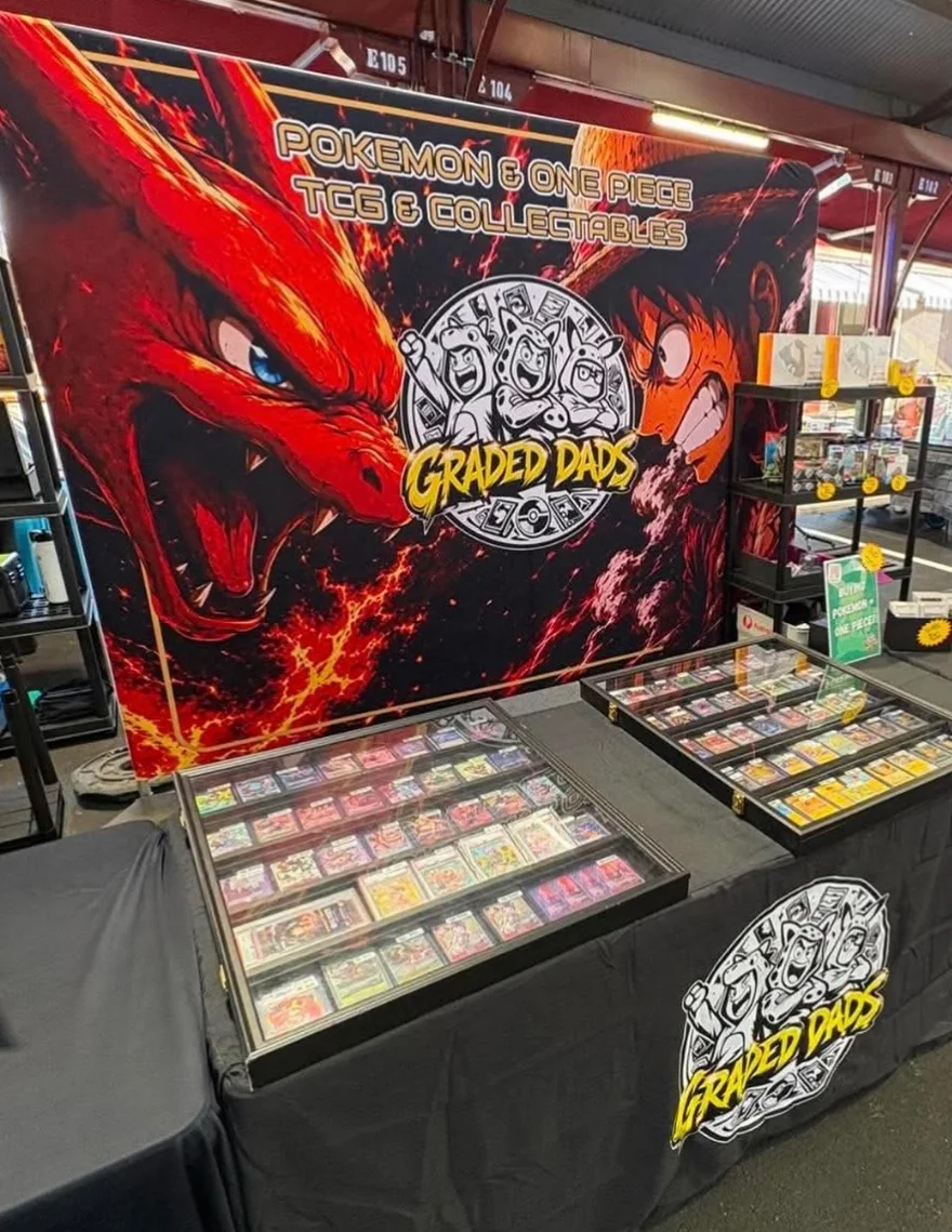 Display cases full of graded cards laid out in front of the Graded Dads banner